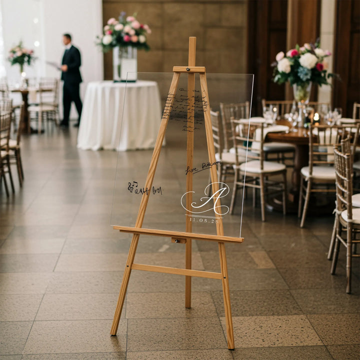 Clear acrylic wedding guest book with monogram A and date on wooden easel in elegant reception venue