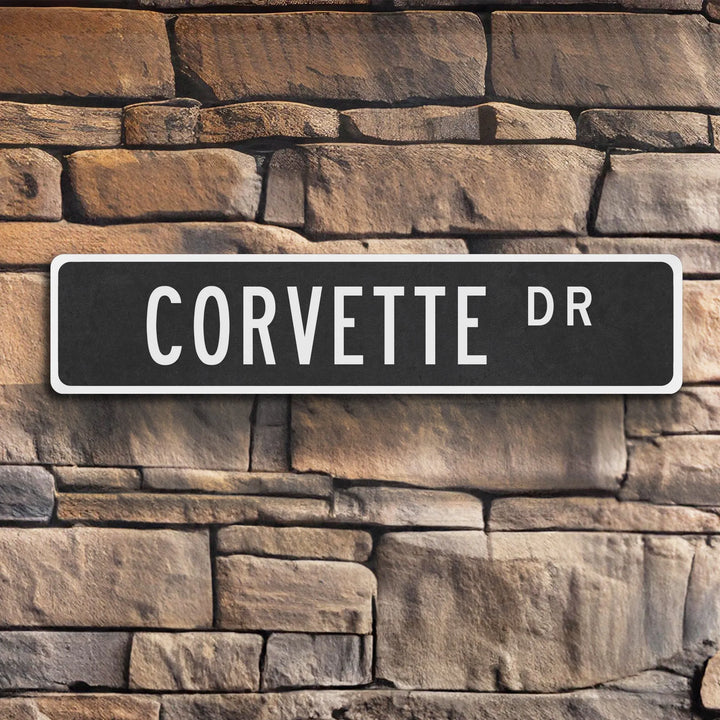 Black metal street sign reading 'CORVETTE DR' mounted on textured stone wall