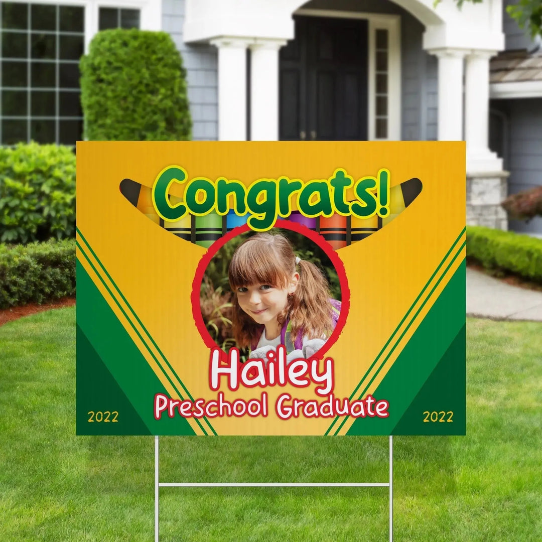 Colorful congratulatory yard sign with crayons design, photo frame, and text for preschool graduate Hailey in front yard