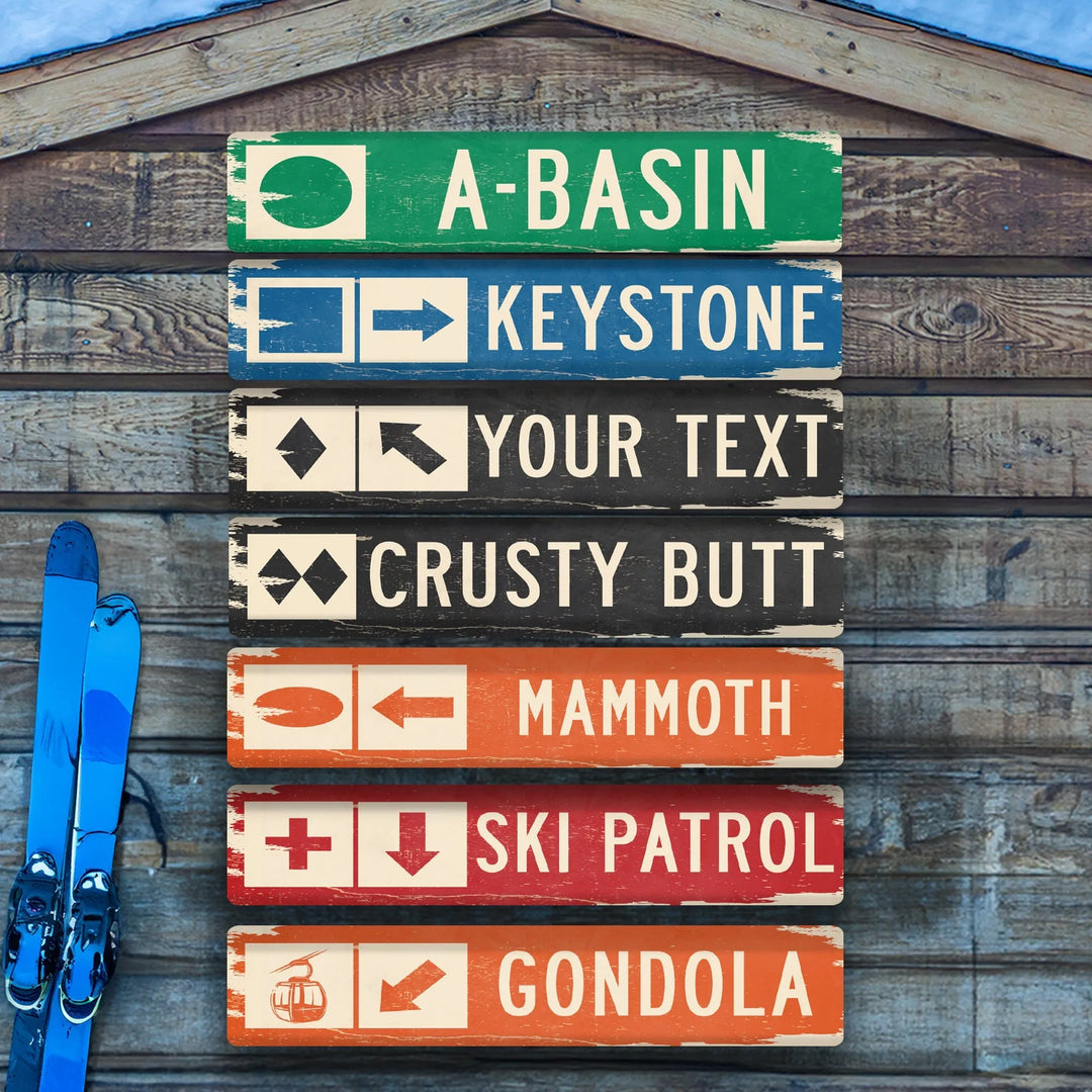 Wooden ski trail sign with directions to A-Basin, Keystone, Crusty Butt, Mammoth, Ski Patrol, Gondola next to blue skis