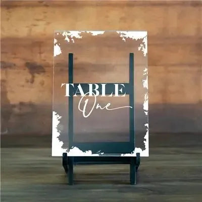 Deckled edge acrylic table number sign reading 'Table One' on black stand with rustic wooden background