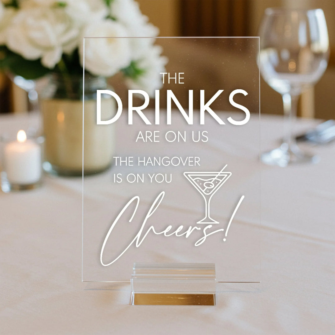 Clear acrylic wedding table sign with message about drinks and hangover on white tablecloth with flowers and glassware