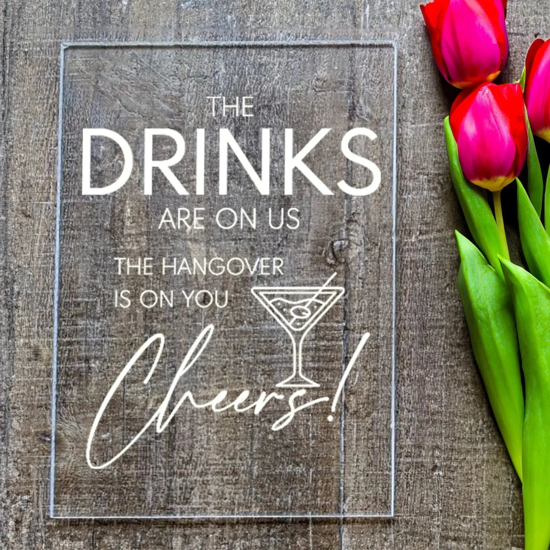 Clear wedding table sign with drink-related quote on wood background and red tulips