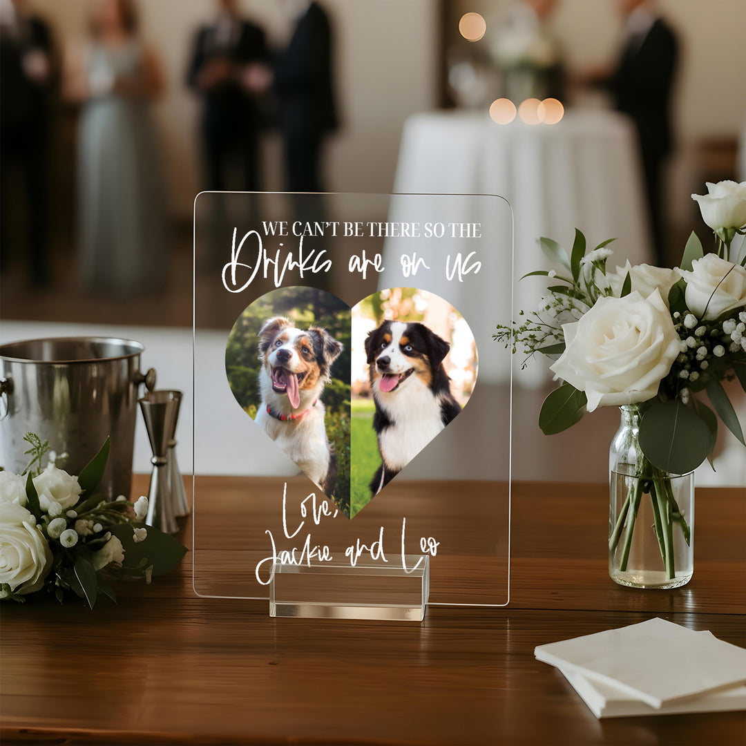 Acrylic sign with dogs' photos and text on a table with flowers and a bucket.