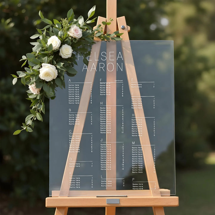 Clear acrylic wedding seating chart on wooden easel with white roses and greenery decoration