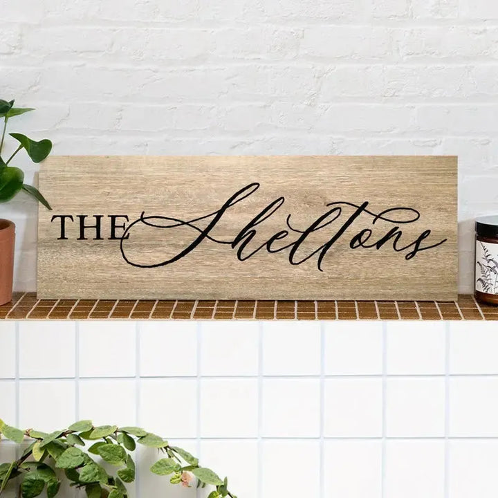 Custom wood family last name sign on shelf with plants and white brick background