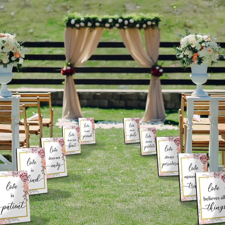 Outdoor wedding aisle with floral vases and signs featuring Corinthians love quotes and beige draped arch