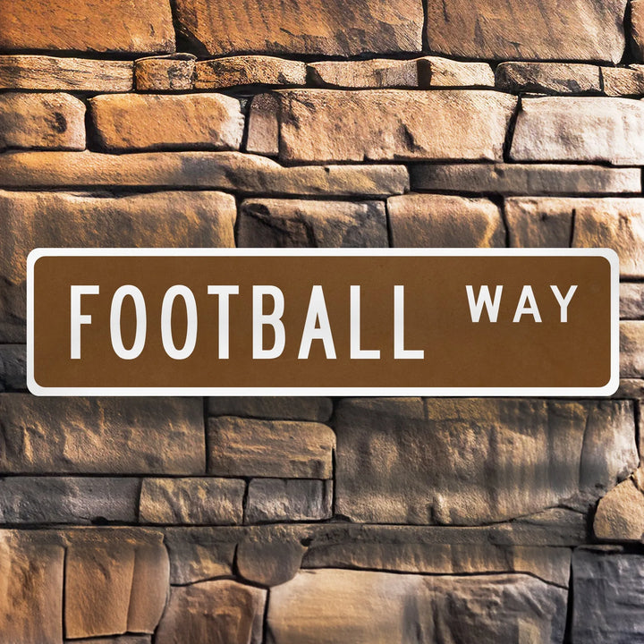Brown metal street sign reading 'FOOTBALL WAY' mounted on textured stone wall