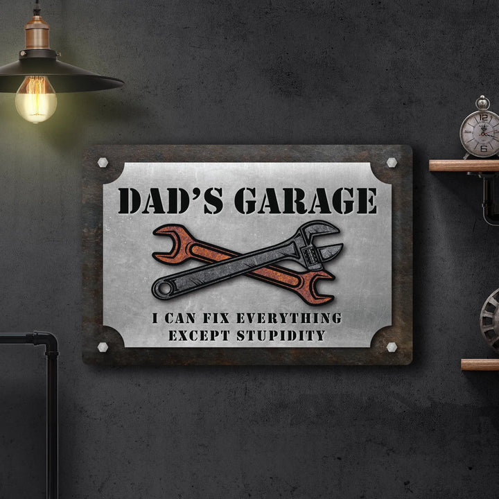 Metal sign in a garage with crossed wrench and spanner, text Dad's Garage can fix everything except stupidity