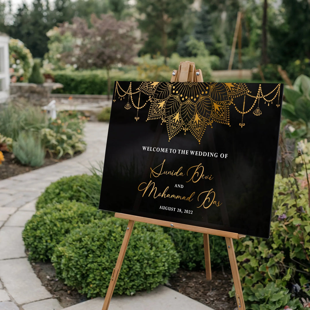 Elegant black and gold Indian wedding welcome sign with floral mandala, outdoor garden setting