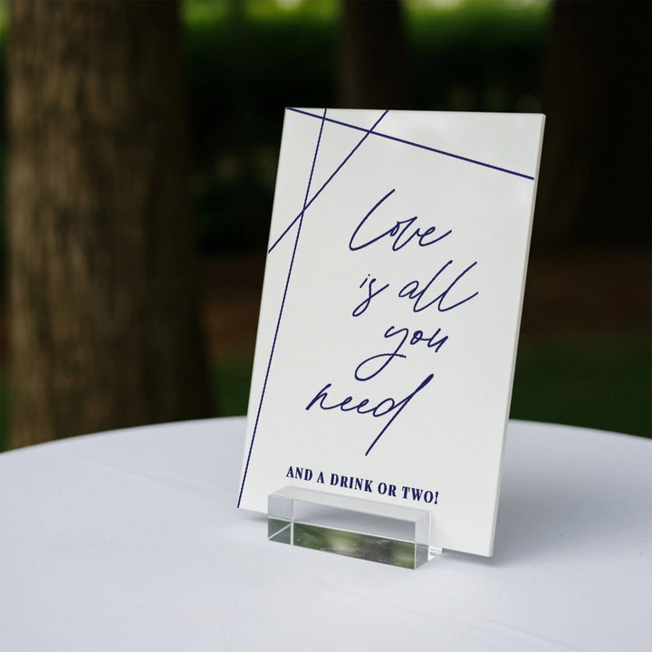 Geometric wedding bar sign on acrylic stand reading Love is all you need and a drink or two