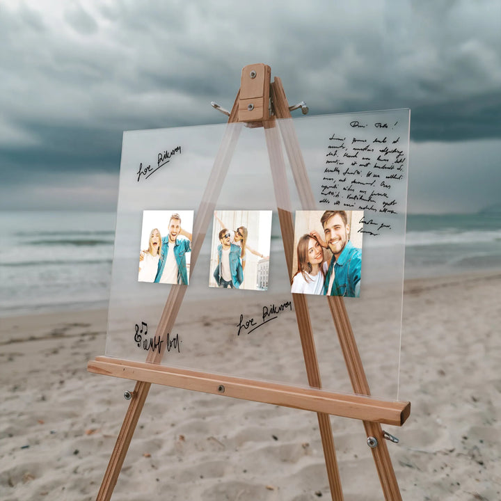 Clear acrylic guest book with photos and handwritten notes on wooden easel at beach with cloudy sky