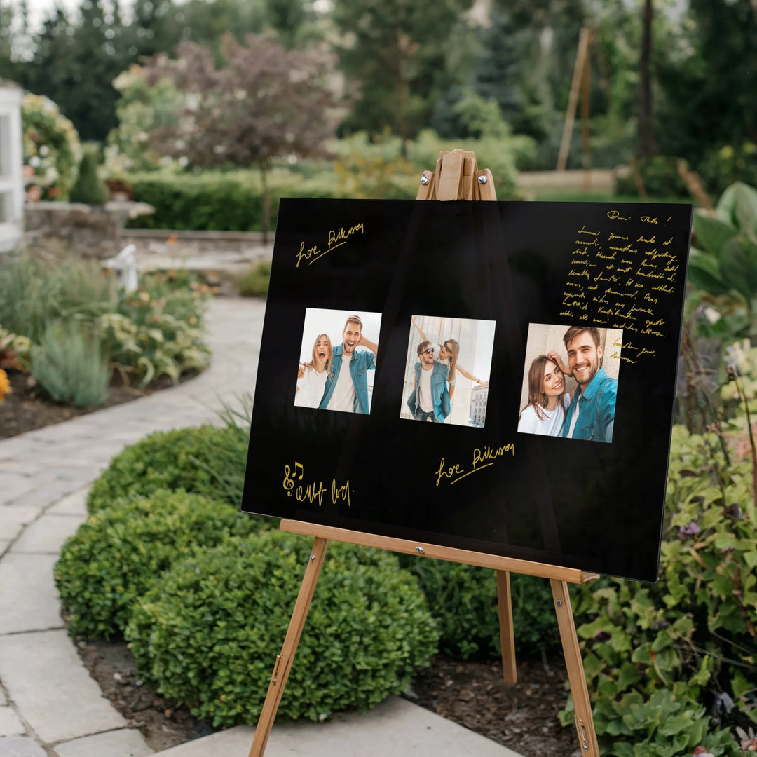 Black guest book sign on wooden easel with handwritten gold messages and three couple photos outdoors