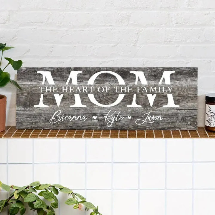 Rustic wooden sign with 'MOM the heart of the family' in white text, on a tiled shelf