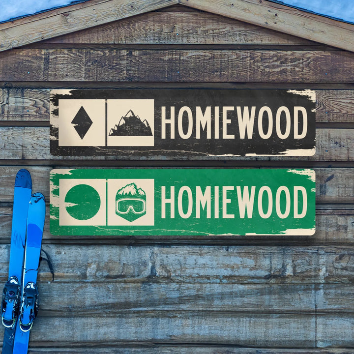 Distressed metal ski trail signs with Homiewood text and mountain symbols on wooden background