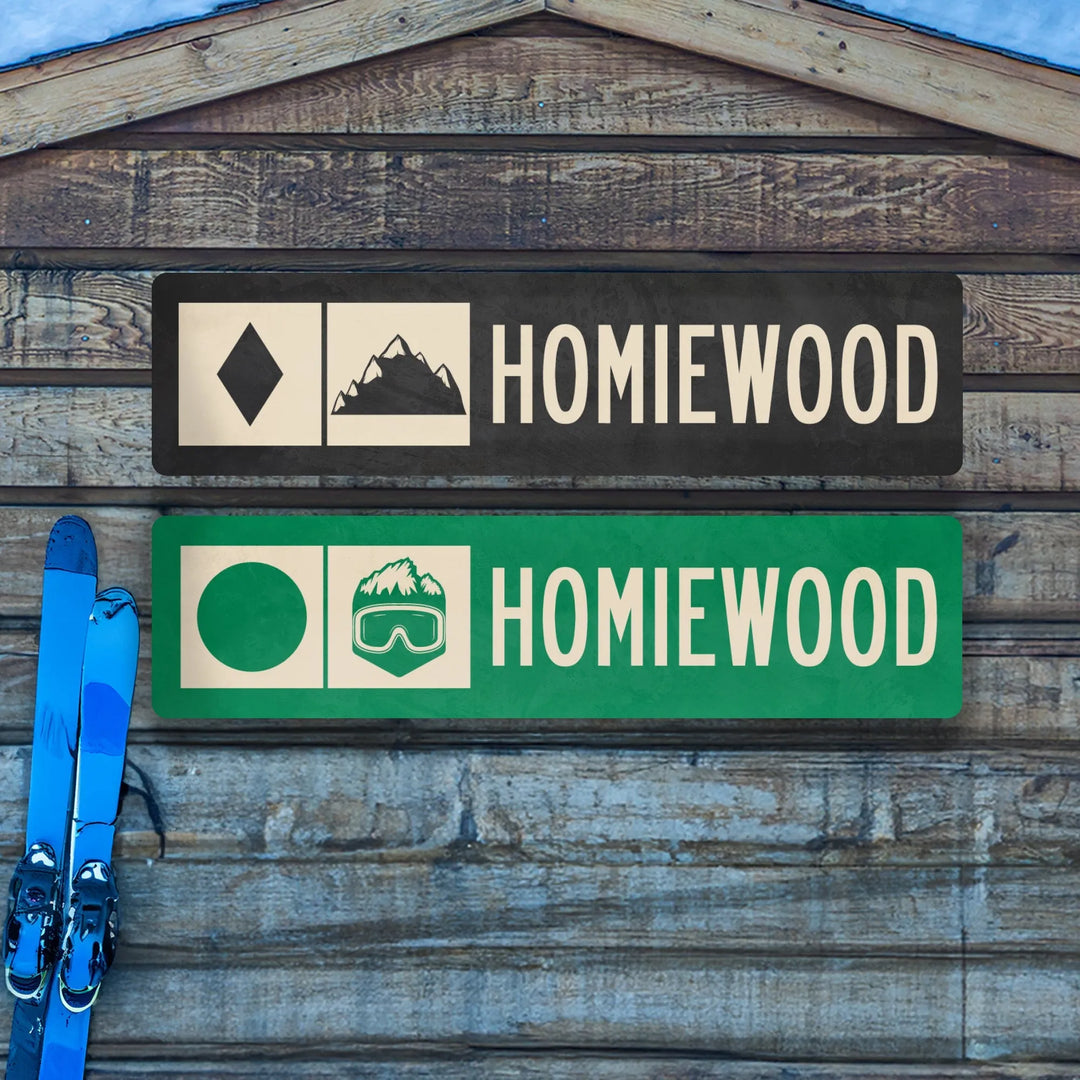 Two rectangular Homiewood ski trail metal signs on rustic wood wall with blue skis leaning on the side