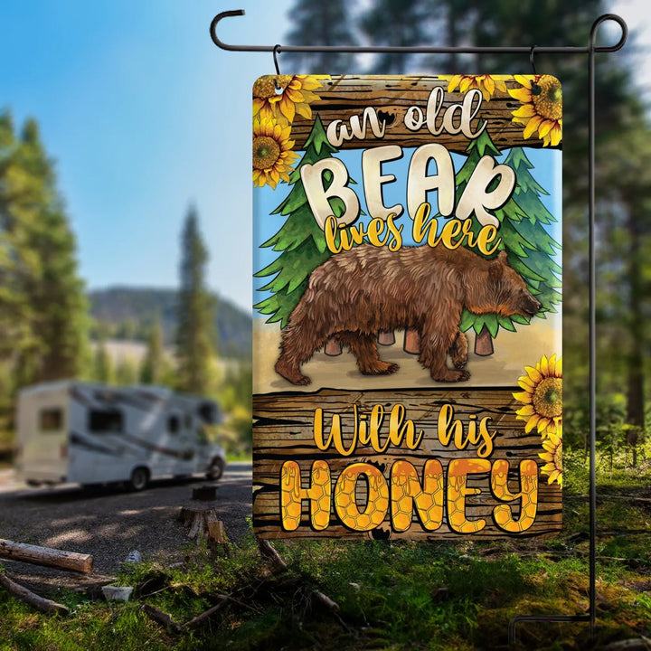 Garden flag with a brown bear walking, pine trees, sunflowers, and text 'an old bear lives here with his honey'