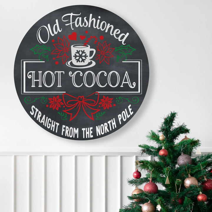 Round black Christmas metal sign with Old Fashioned Hot Cocoa text and festive decorations near decorated Christmas tree