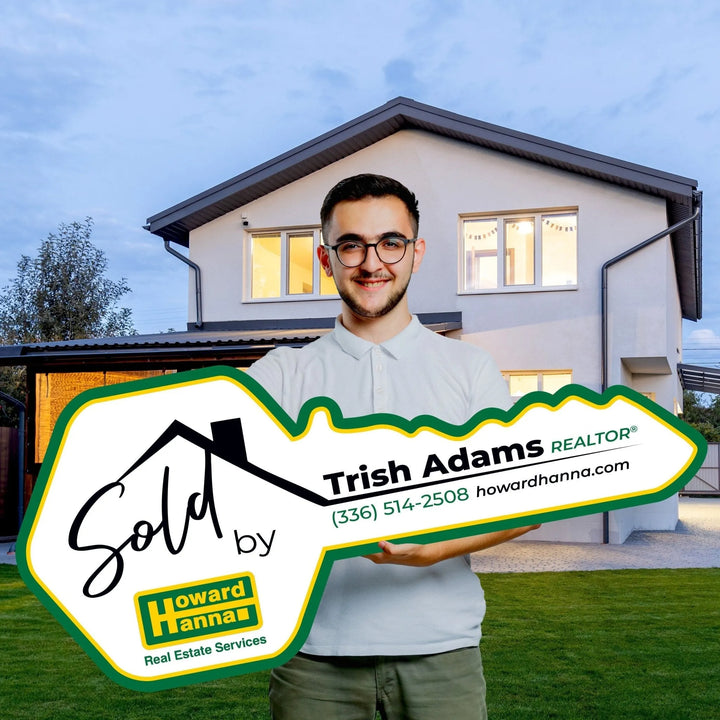 Smiling man holding large key-shaped sign for Trish Adams Realtor Howard Hanna in front of modern house