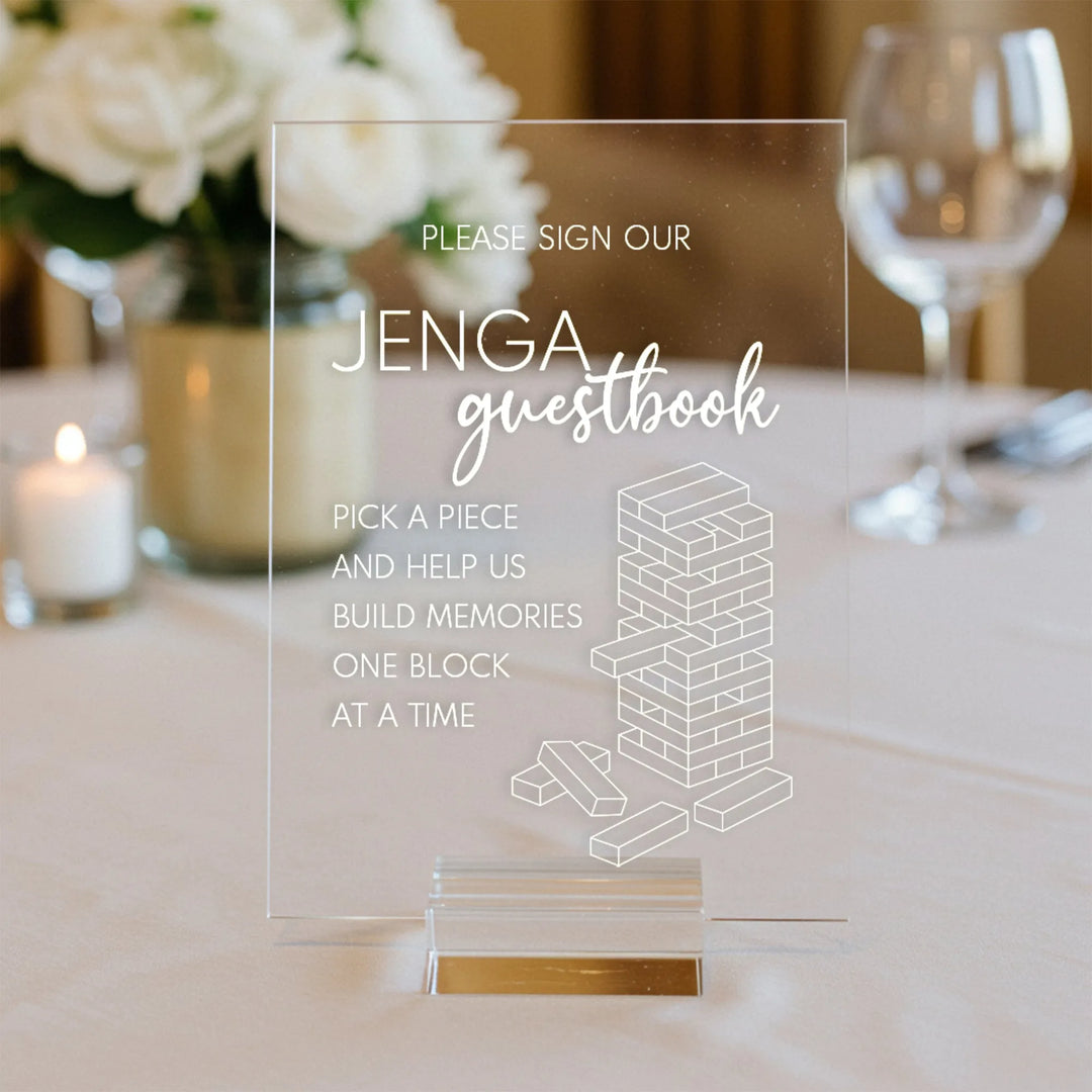 Clear acrylic Jenga guestbook sign on wedding table with floral centerpiece, candle, and wine glass