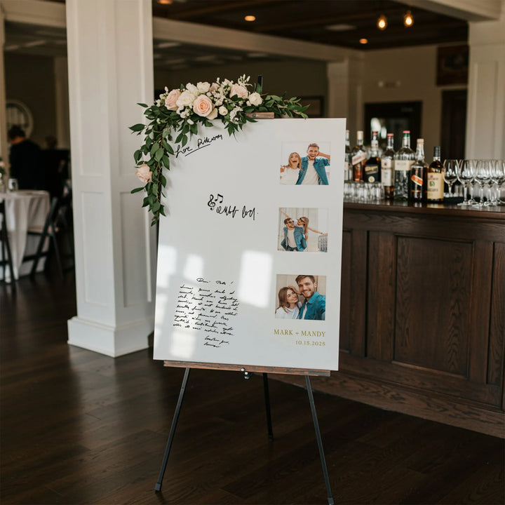 Wedding guest book sign with floral decoration, photos of couple, and bar in background