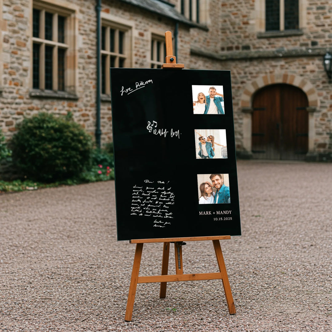 Black wedding guest book sign with photos and handwritten messages on wooden easel outside stone building