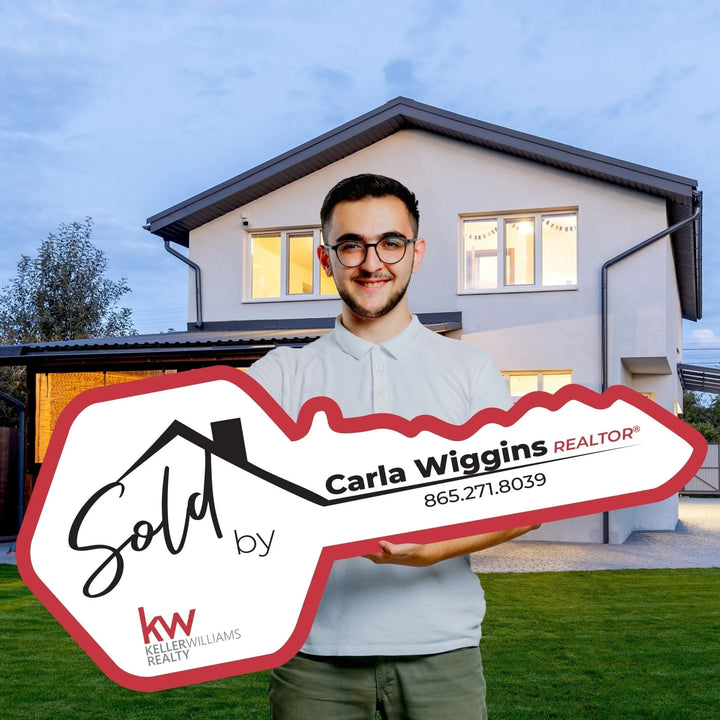 Smiling man holding large key-shaped real estate sign in front of modern house at dusk