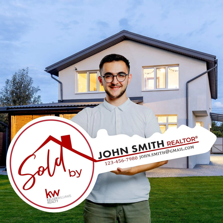 Smiling man holding large sale key sign for John Smith Realtor in front of modern house lawn