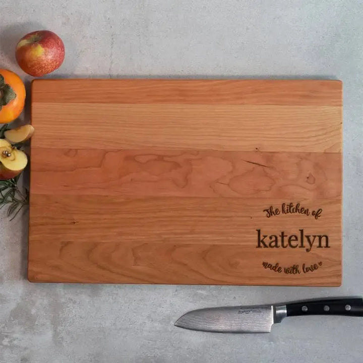 Personalized wooden cutting board in kitchen with knife, fruit, and engraved name 'katelyn'.