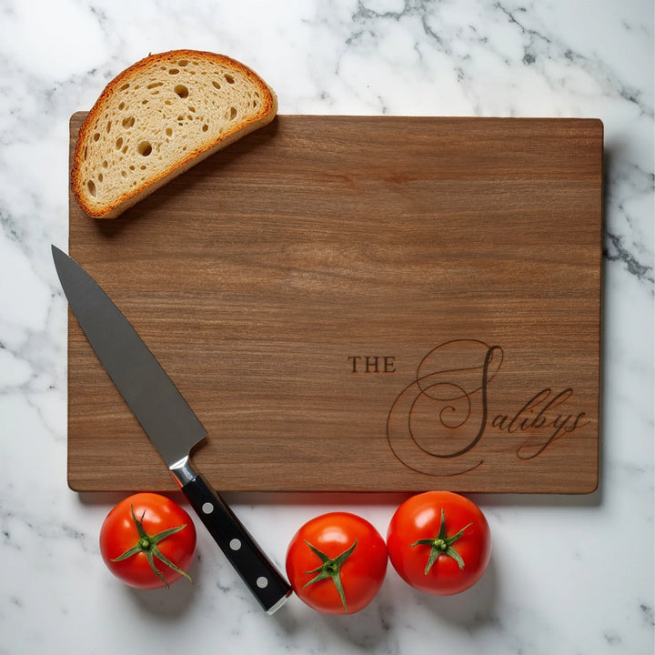 Personalized last name cutting board with bread, knife, and tomatoes on marble counter
