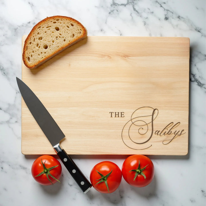 Personalized wooden cutting board with bread slice, knife, and three tomatoes on marble