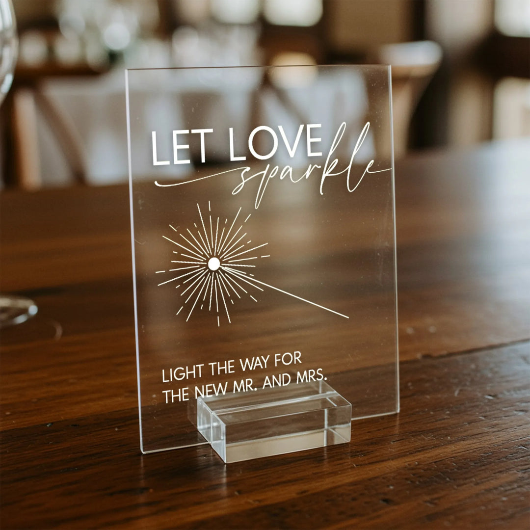 Clear acrylic wedding table sign reading Let Love Sparkle with sparkler graphic on wooden table