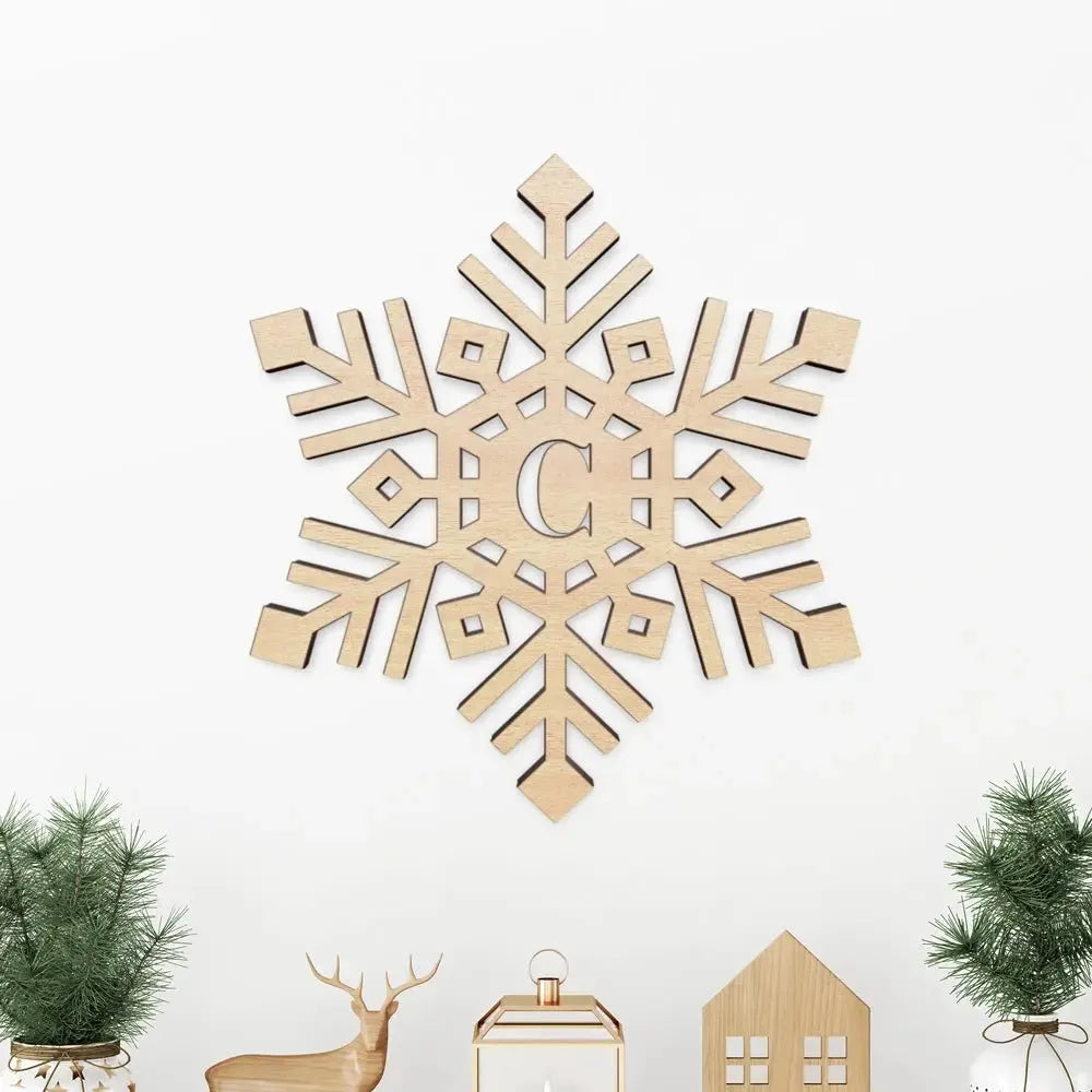 Wooden monogram snowflake sign with letter C, holiday decor, on white wall above mini trees.