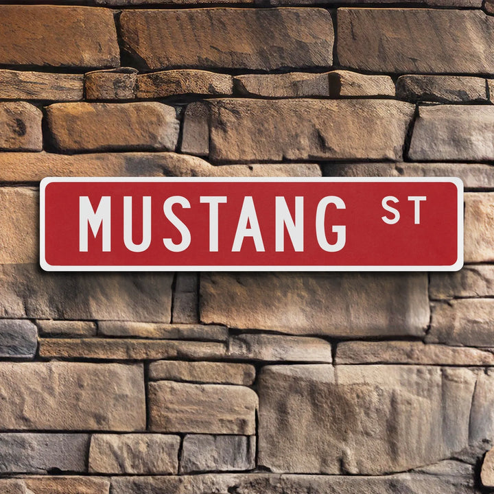 Red metal street sign reading Mustang St mounted on rustic brown stone wall