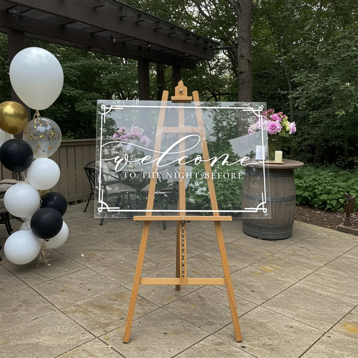 Elegant acrylic welcome sign on wooden easel with balloons and outdoor garden setting