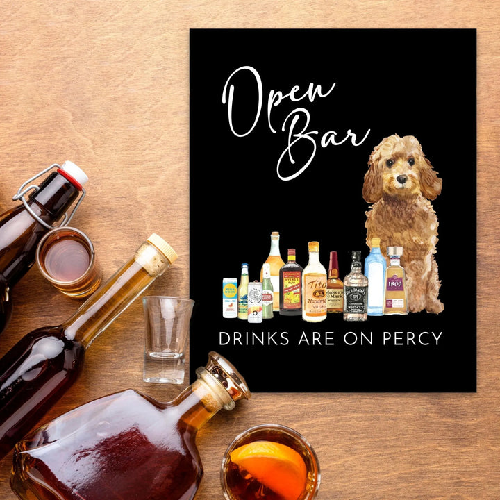 Black open bar sign with illustrated dog and assorted liquor bottles on wooden table