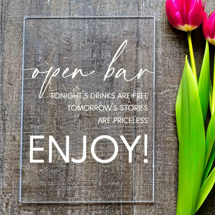Clear acrylic open bar sign with white text on rustic wood background, pink tulips beside