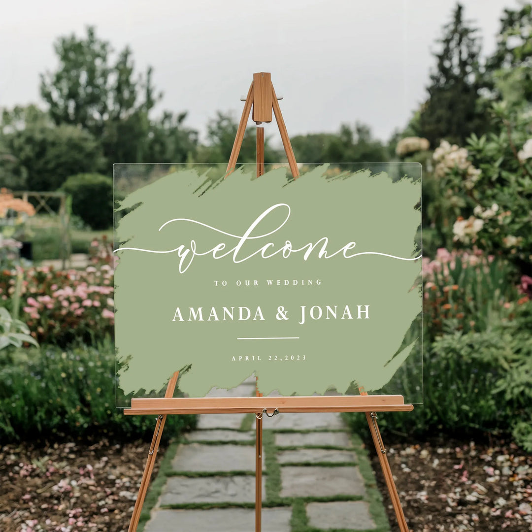 Acrylic wedding welcome sign with green paint swatch and white text on wooden easel in garden