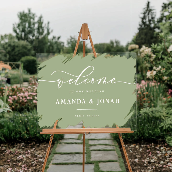 Acrylic wedding welcome sign with green paint swatch and white text on wooden easel in garden