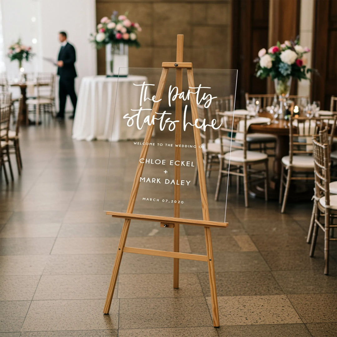 Transparent wedding welcome sign on wooden easel with floral centerpieces and tables in elegant venue