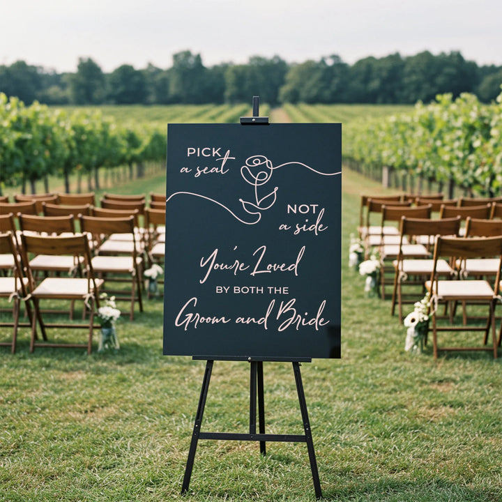 Wedding welcome sign saying 'Pick a seat not a side' in vineyard ceremony setting with wooden chairs