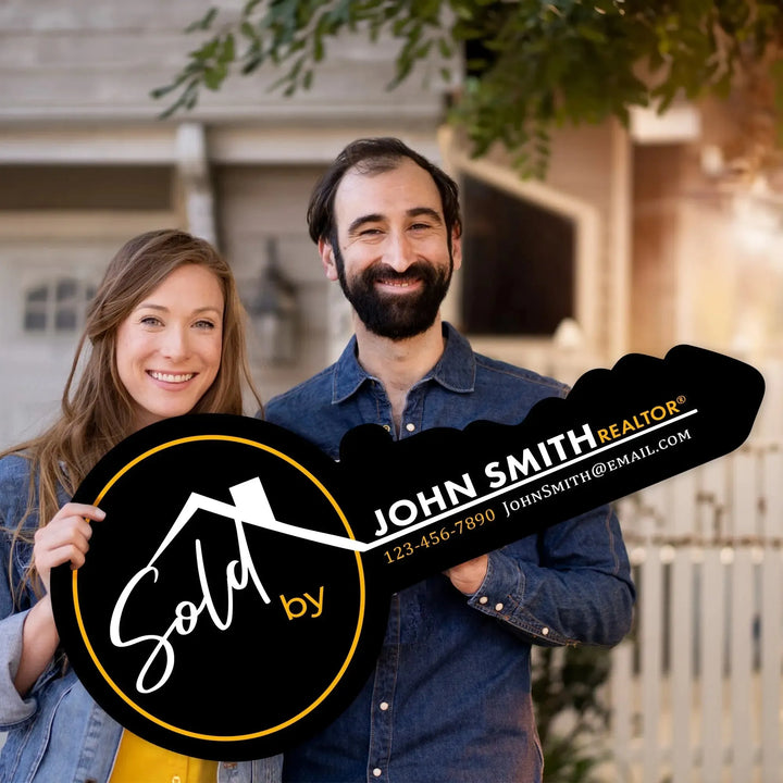 Happy couple holding large black key-shaped real estate sign reading Sold by John Smith Realtor