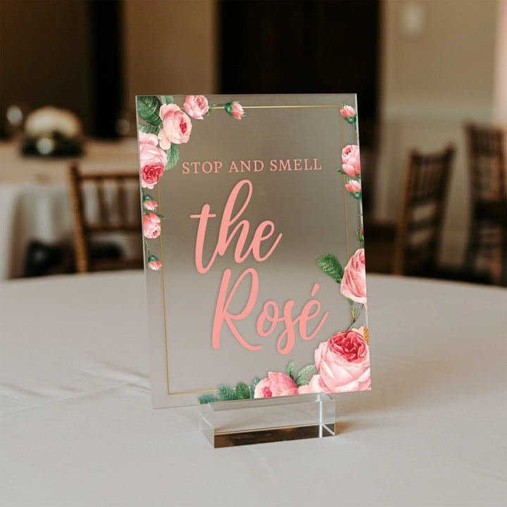 Elegant wedding table sign with pink roses and text 'Stop and smell the Rosé' on clear acrylic