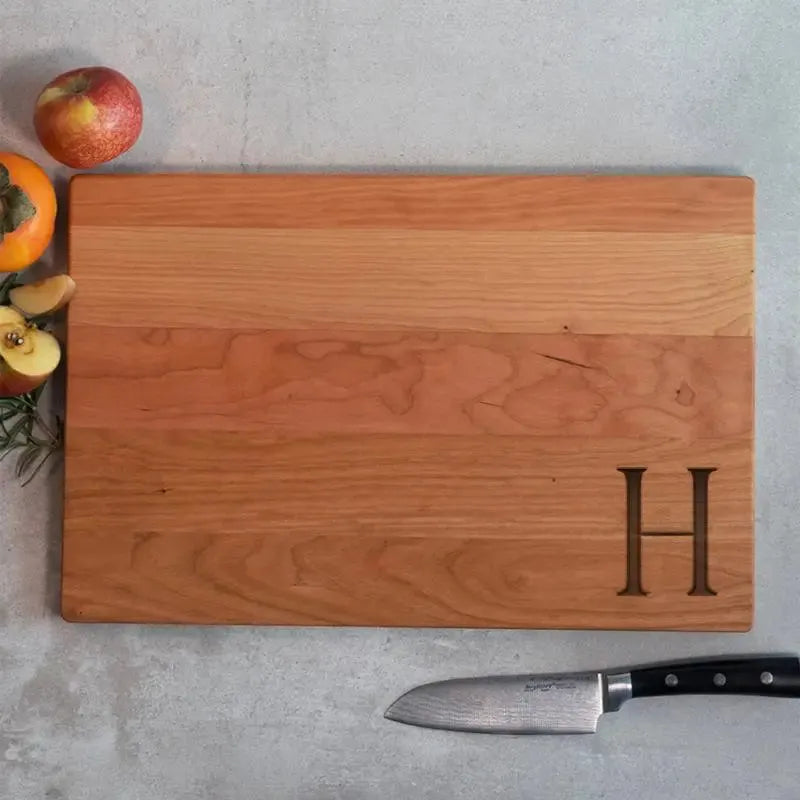 Personalized wood cutting board with engraved letter H, fruits and knife on concrete surface