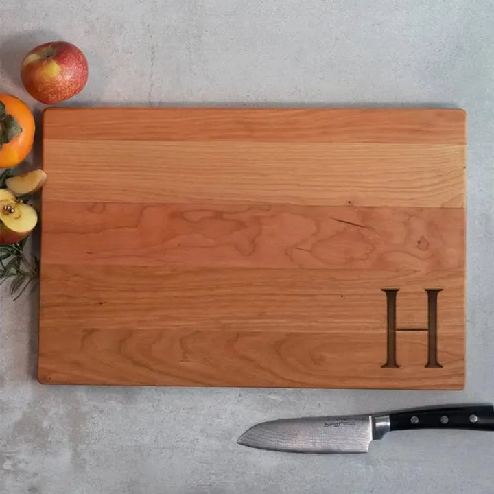 Personalized wood cutting board with engraved letter H, fruits and knife on concrete surface
