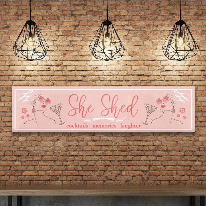 Pink She Shed metal sign with cocktails, memories, laughter text and woman with sunglasses illustration on brick wall