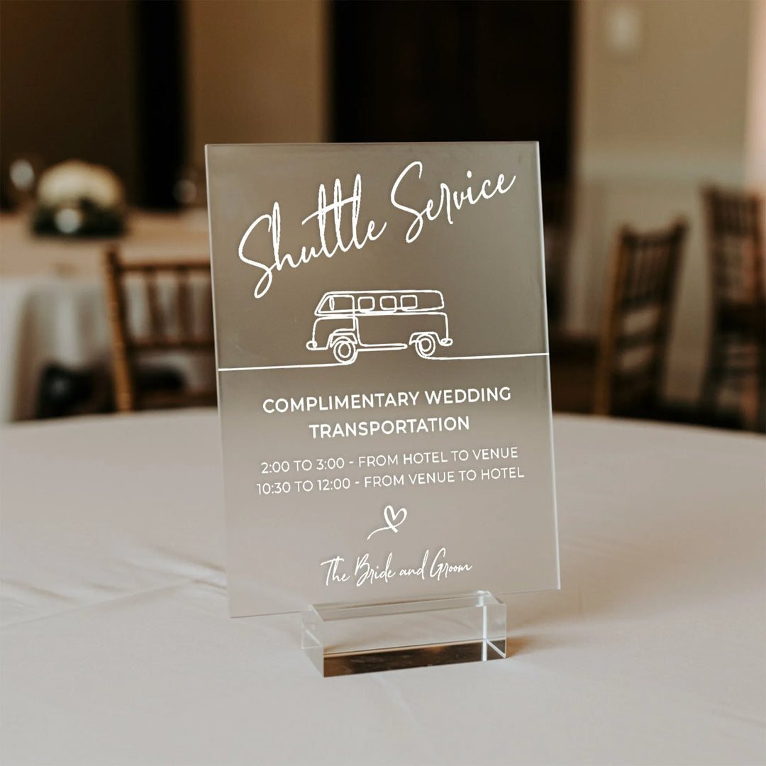 Clear acrylic wedding shuttle service sign with white text and van illustration on table