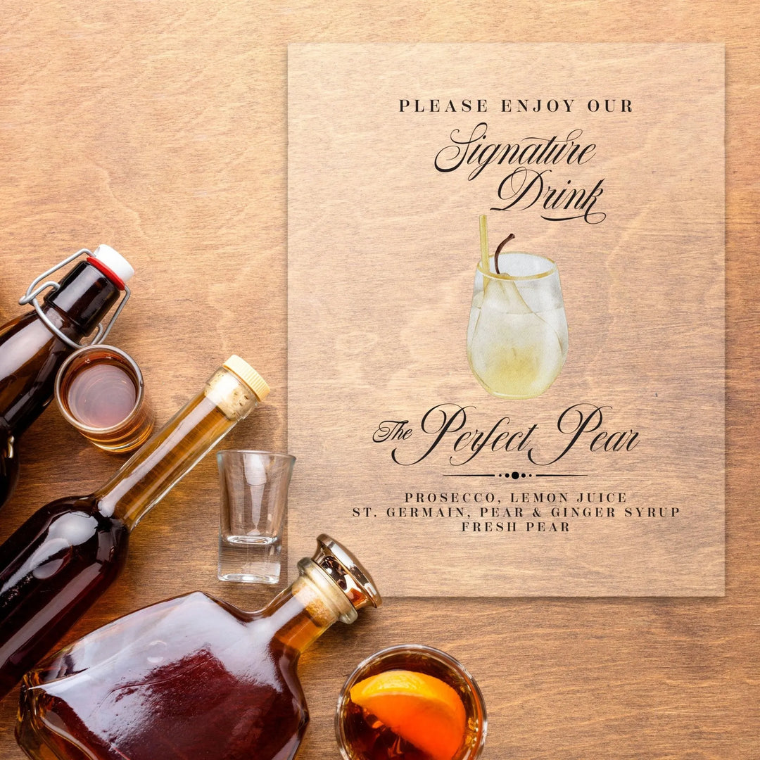 Cocktail ingredients with bottles and glasses beside a wooden sign for The Perfect Pear signature drink