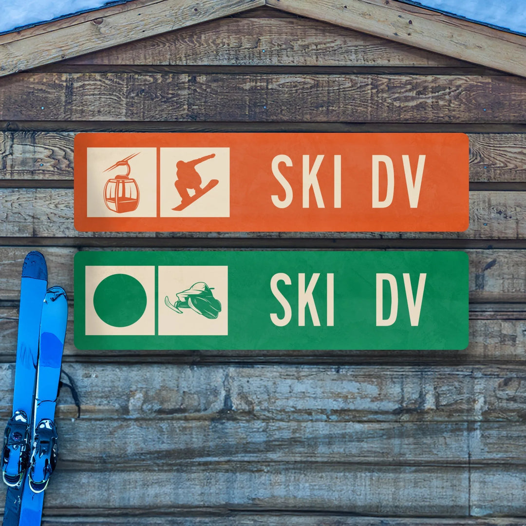 Wooden ski trail signs with ski lift and snowboard icons in orange, snowmobile and green circle icons in green, blue skis leaning on wall