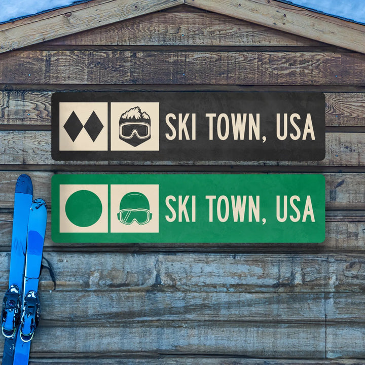 Two Ski Town, USA metal trail signs on wooden wall with blue skis leaning beside them